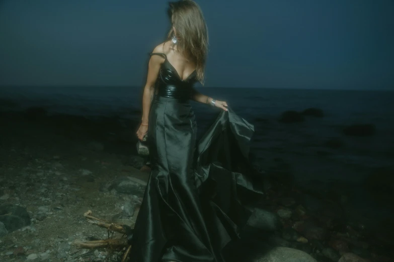 a woman wearing a black dress standing on rocks near the ocean