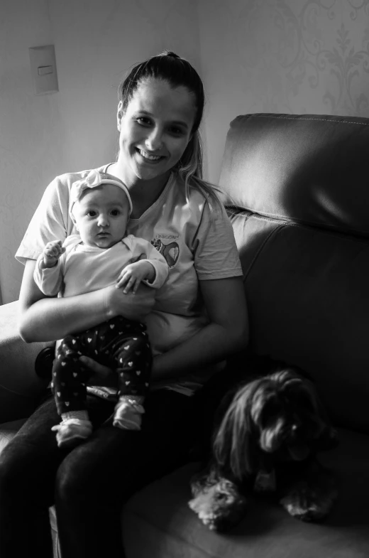 black and white pograph of woman sitting on couch with baby, dog and puppy