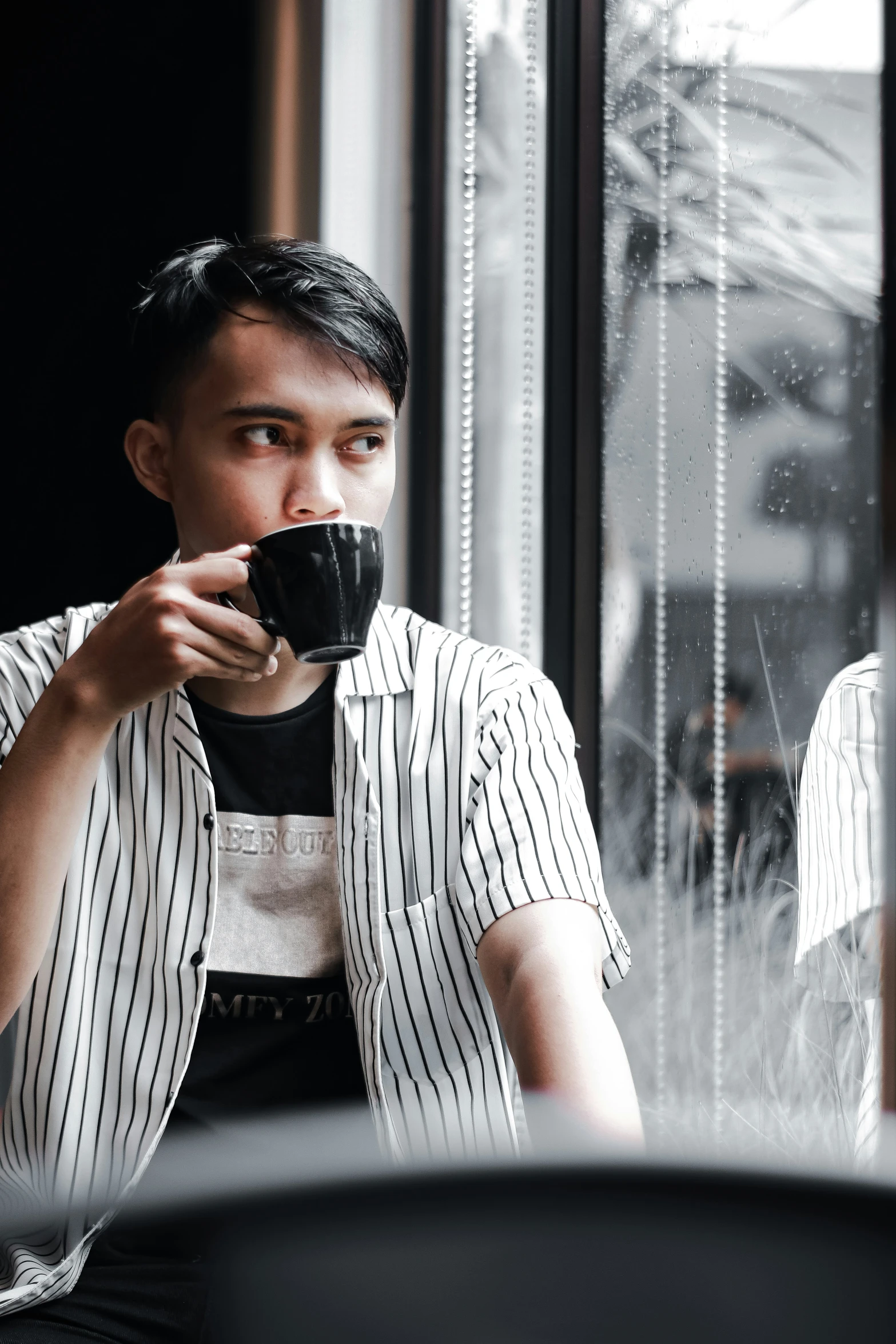 the young man sitting at the table is drinking