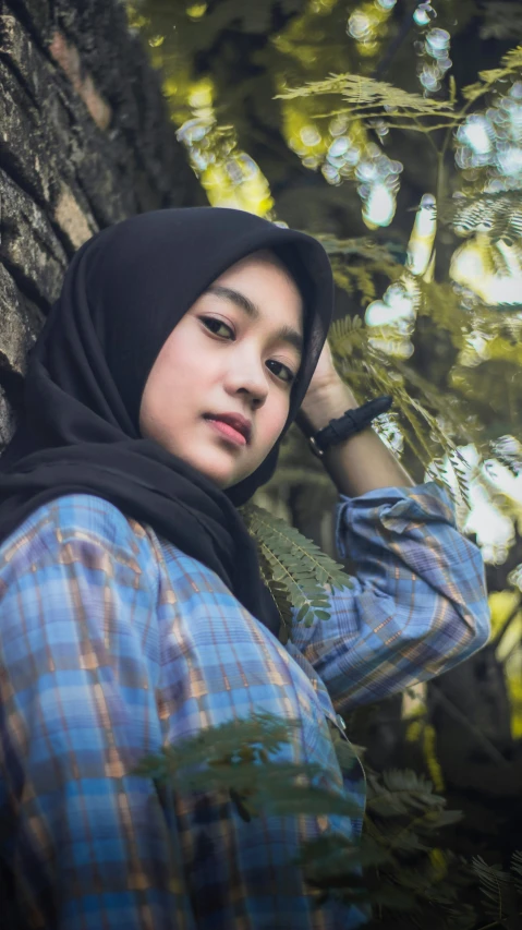 a woman leaning against a tree wearing a hijab