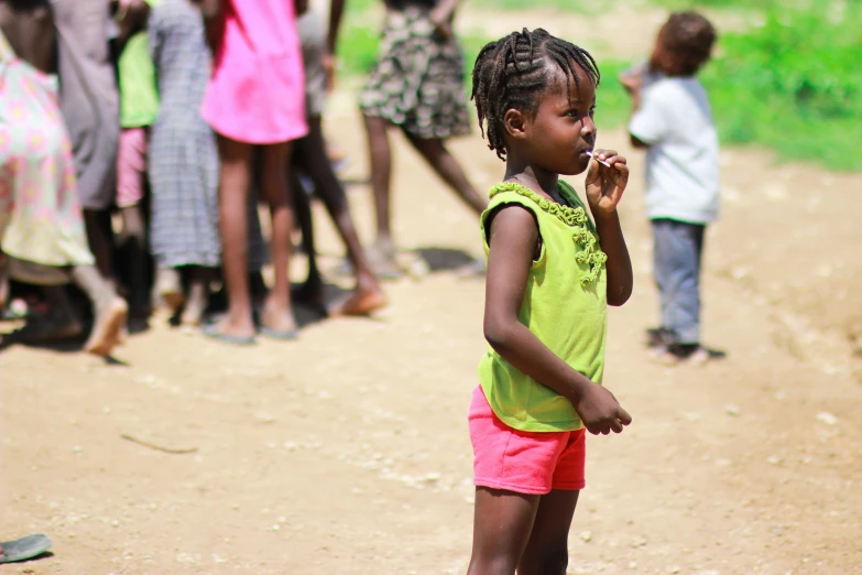 a child stands and watches others in a dirt area