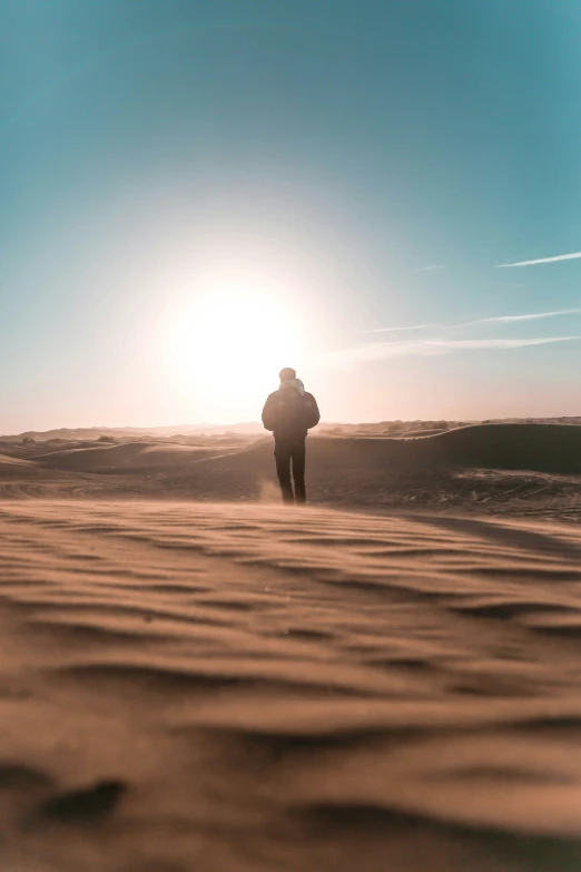 man walking on beach against sunset with the sun behind him