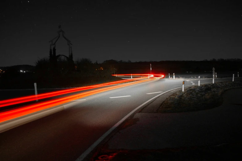 red light trails in the night sky over an empty road