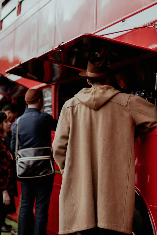 the back of a red double - decker bus with people standing nearby