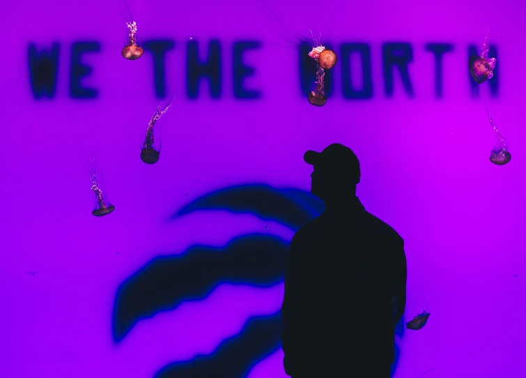 silhouette of a man in a hat near purple wall with words