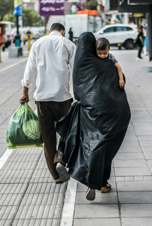 a man carrying a woman in an open bag while walking down the sidewalk