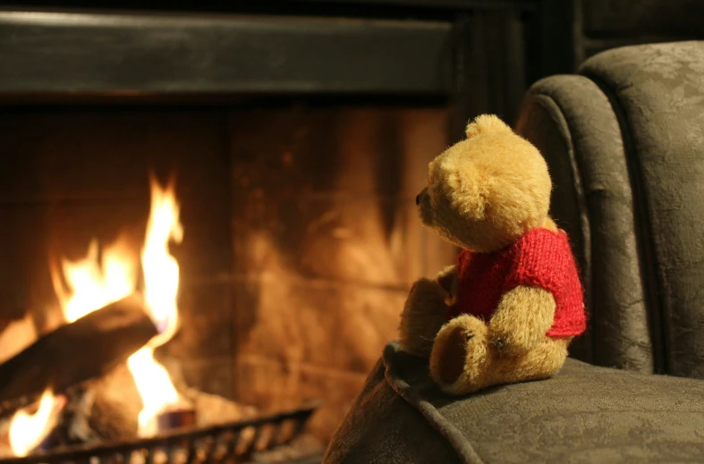 a teddy bear wearing a red sweater sitting in a chair near a fireplace