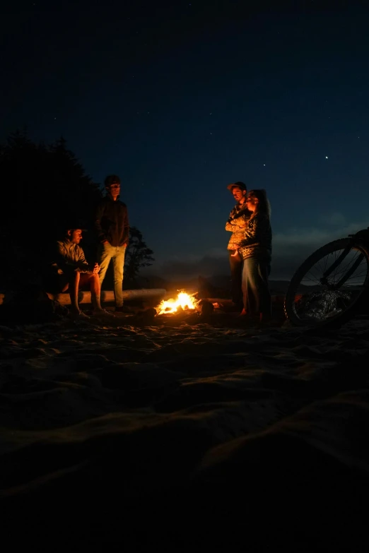 three people are standing next to a campfire while others sit and watch