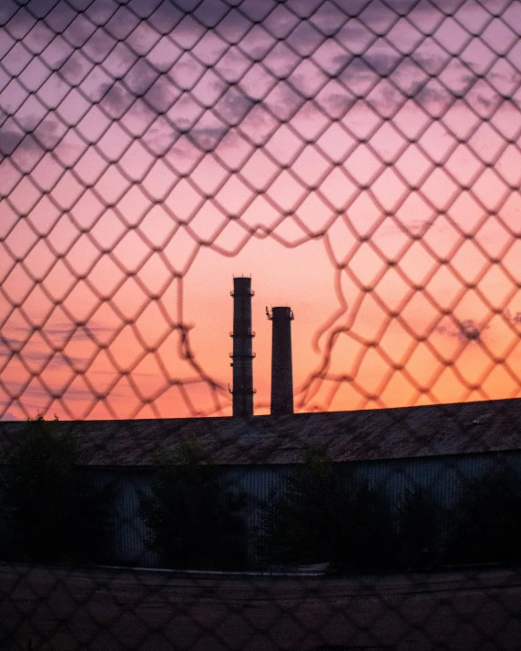 the view through the mesh fence at sunset, with a silhouette of two chimneys