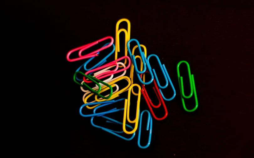 neon colored paper clips sit in a row on a black background