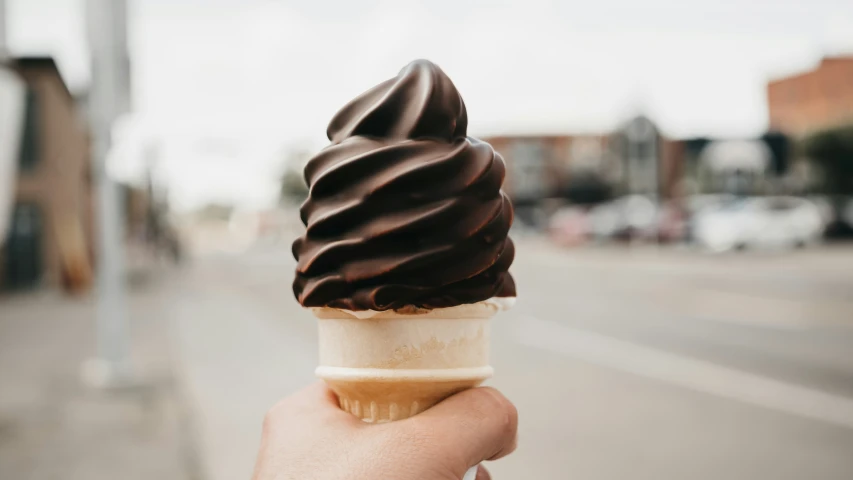 a hand holding up a chocolate covered ice cream cone