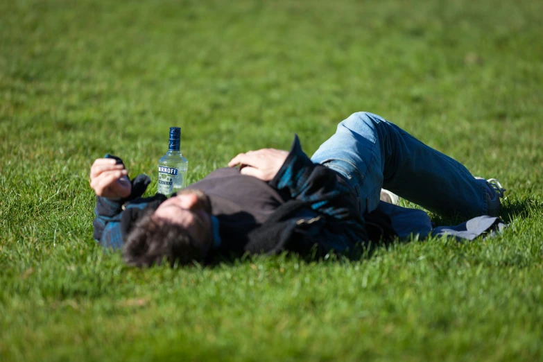 there is a man laying on the grass with an empty bottle in his hand