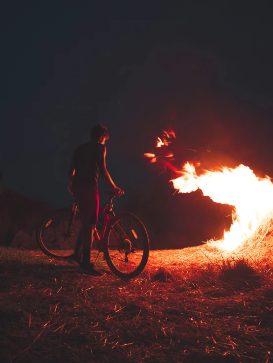 a guy stands by his bike near a big fire