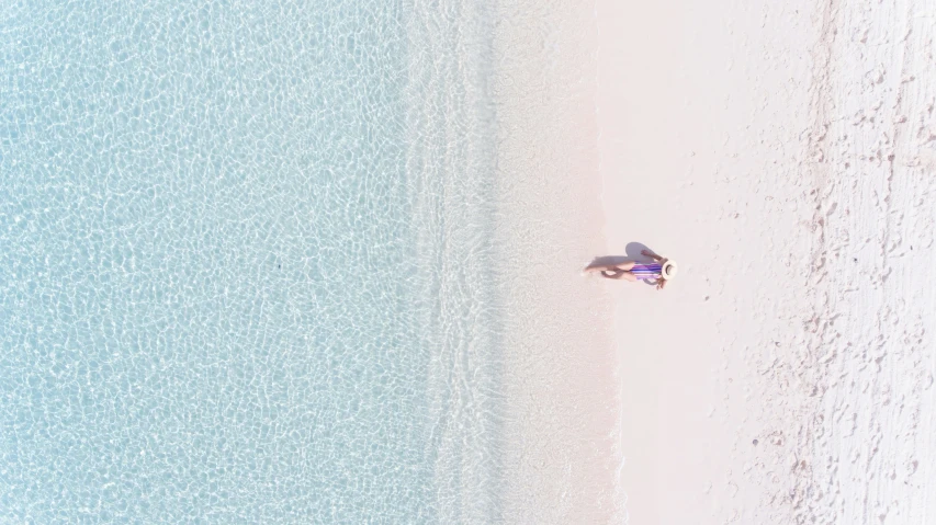 an aerial view shows the sea and beach with a lone person lying on it