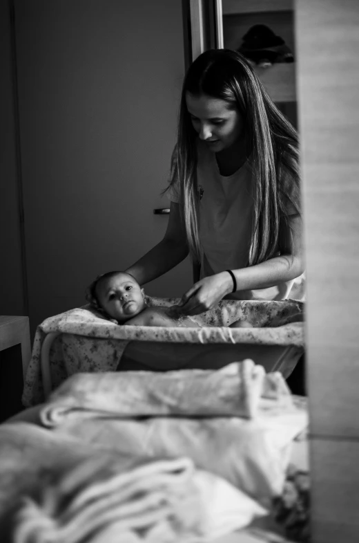a woman standing over a bed while touching the head of a baby