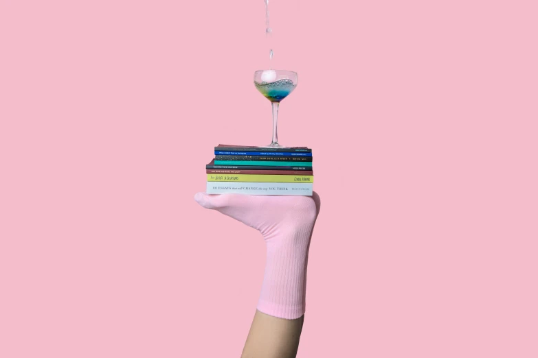 the person is holding a stack of books with a drink on top