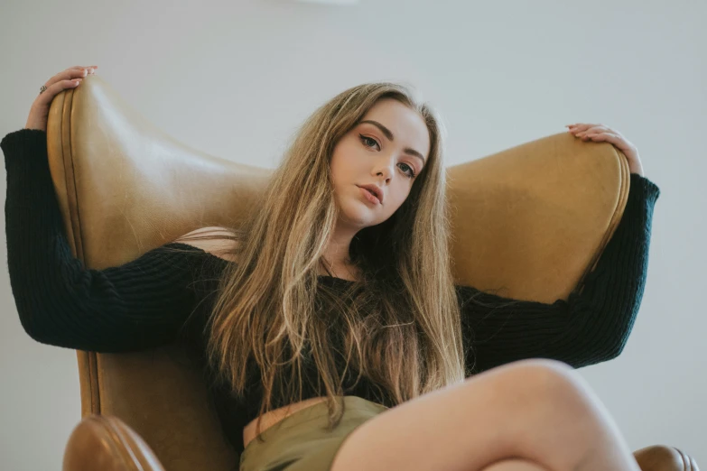 a beautiful young blond sitting on a brown chair