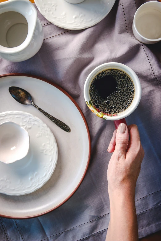 a person holding a cup of coffee in their hand and saucer