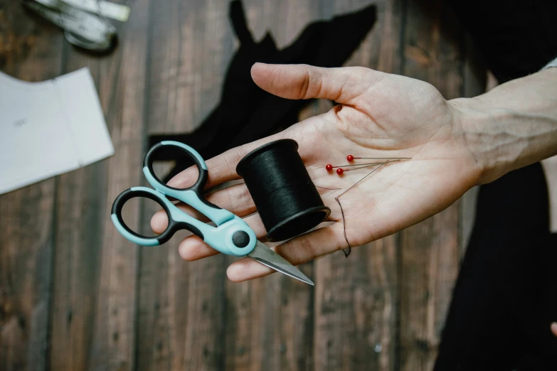 person holding black thread and scissors on top of a table