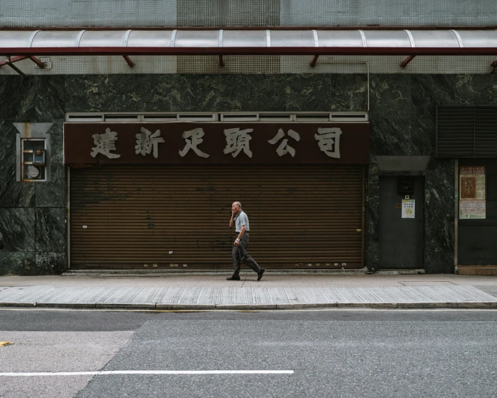 man walking down a sidewalk in front of a building with an asian message painted on it