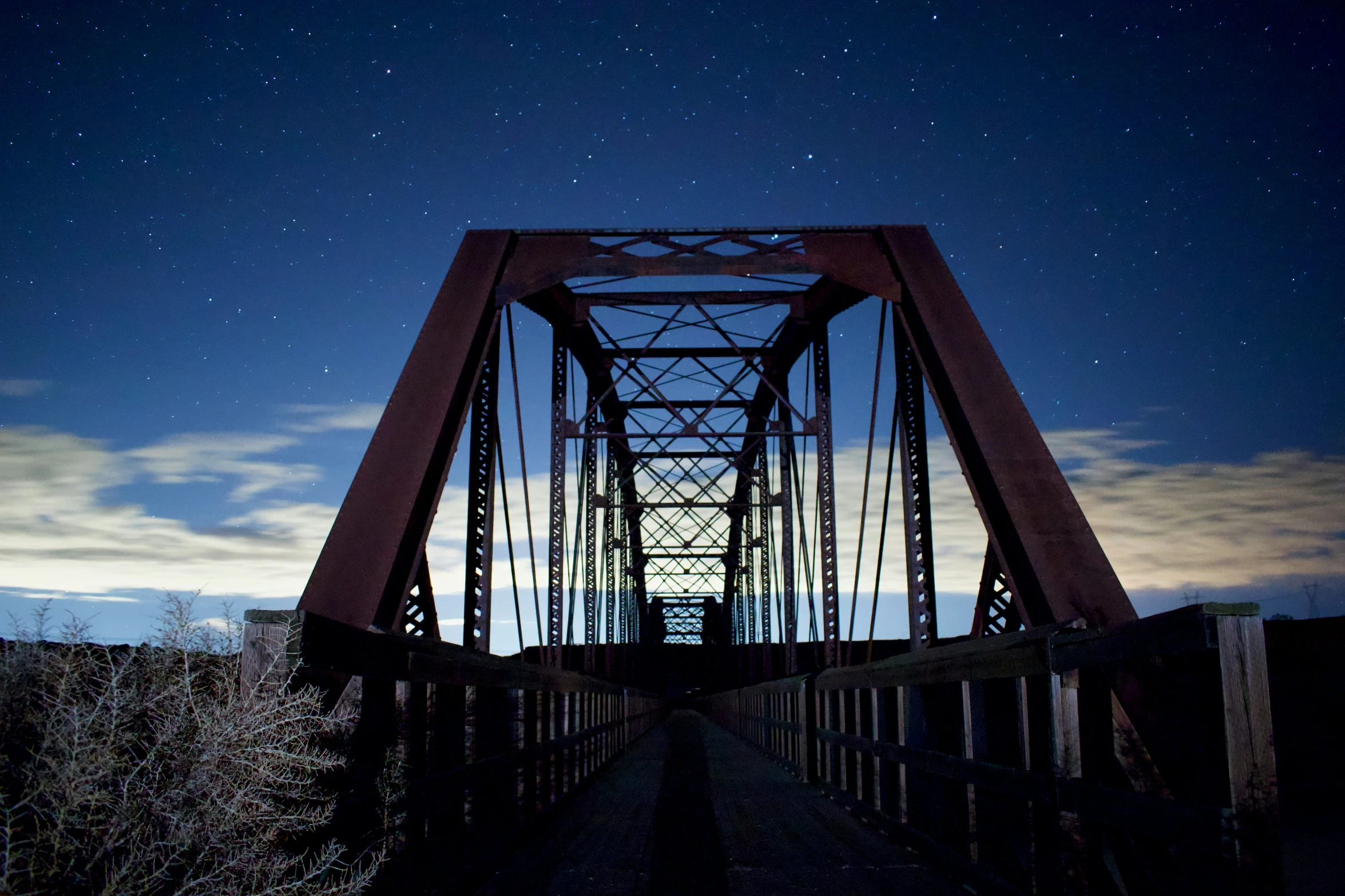 the night sky is lit up behind a long metal bridge