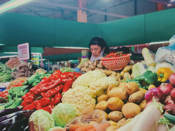 a lady standing behind a lot of vegetables