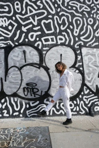 a woman walking past a graffiti wall wearing white