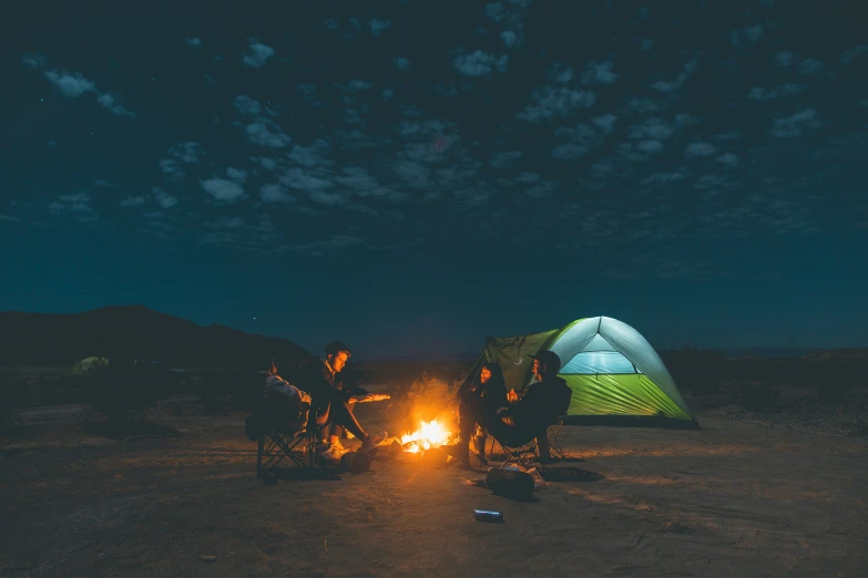 three people sitting around a camp fire near a tent