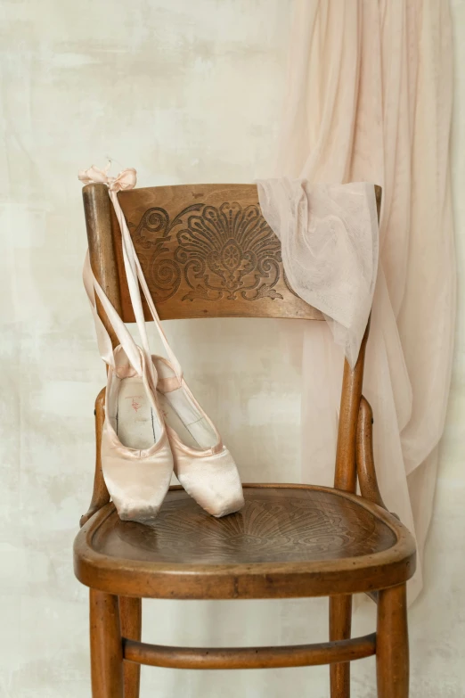 a pair of ballet shoes sit on a wooden chair