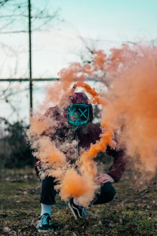 a man in a purple jacket kneeling down by some yellow smoke