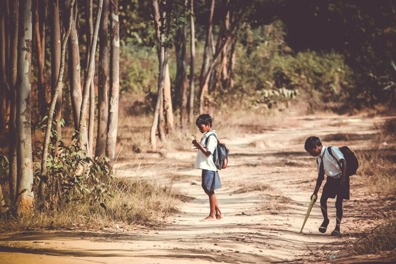 two children carrying skis walk down a dirt road