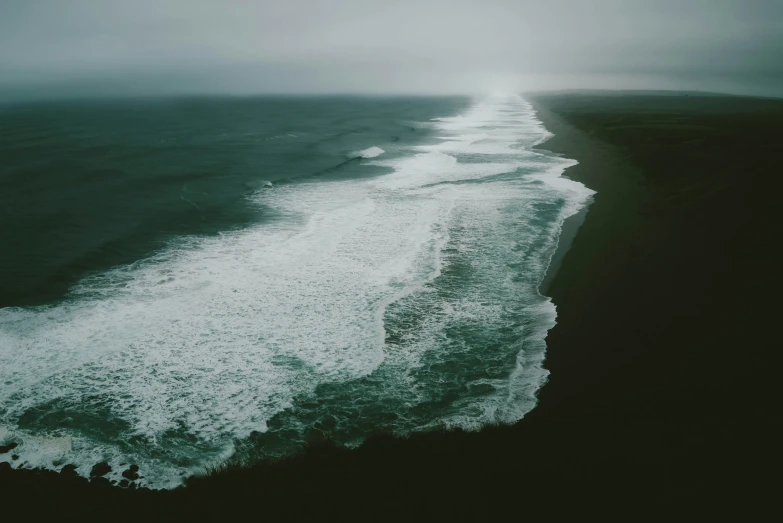 a sandy shore with a wave and an ocean