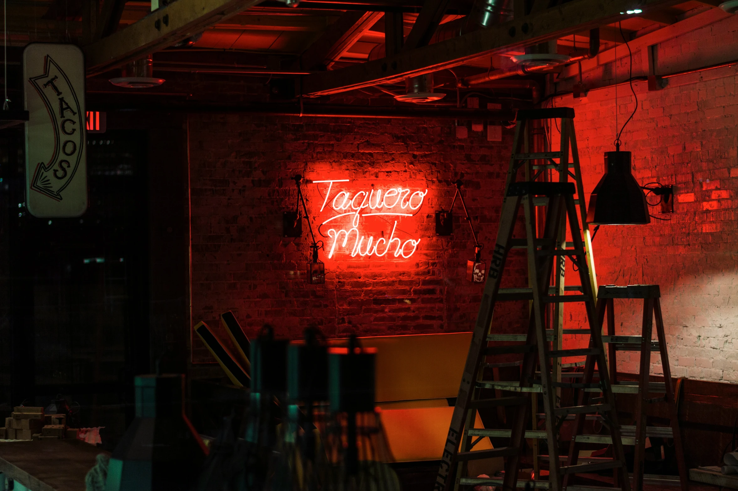 the back room of a restaurant with an old ladder and a red neon sign