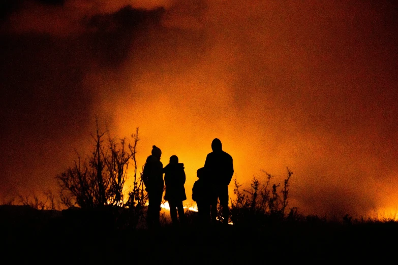 three people standing together in front of a fire