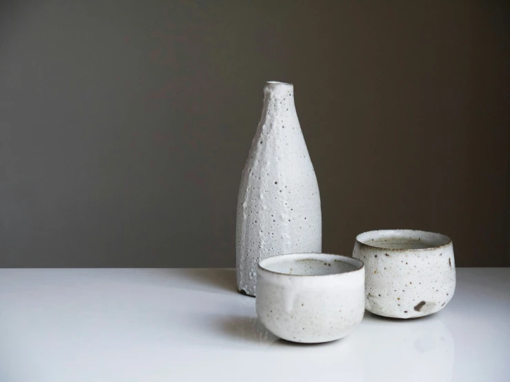 two vases sitting on the floor beside a bowl