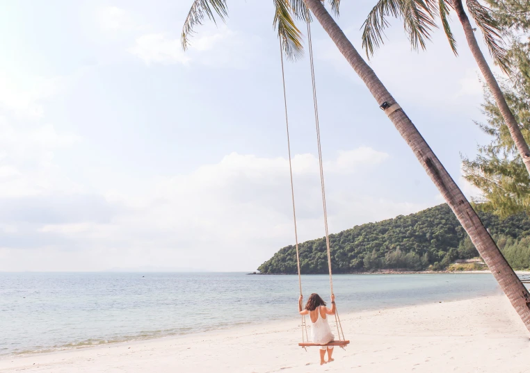 a woman swings on a swing set near the beach