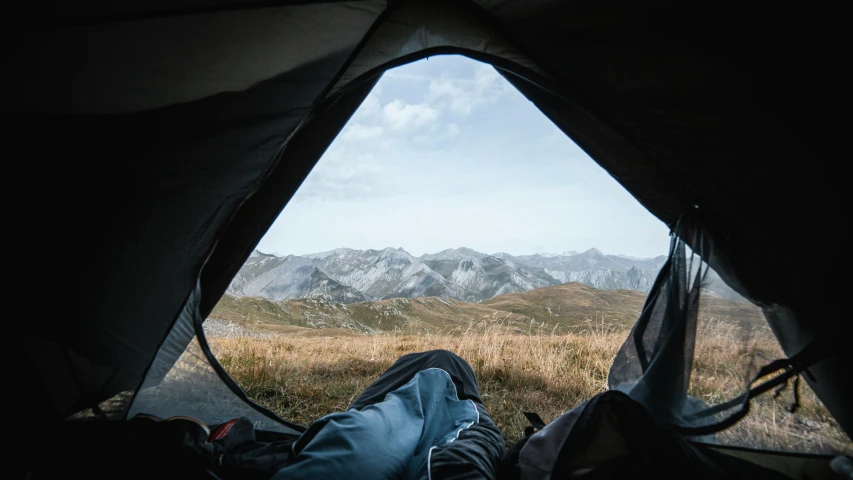 person lying in sleeping tent on rocky hillside