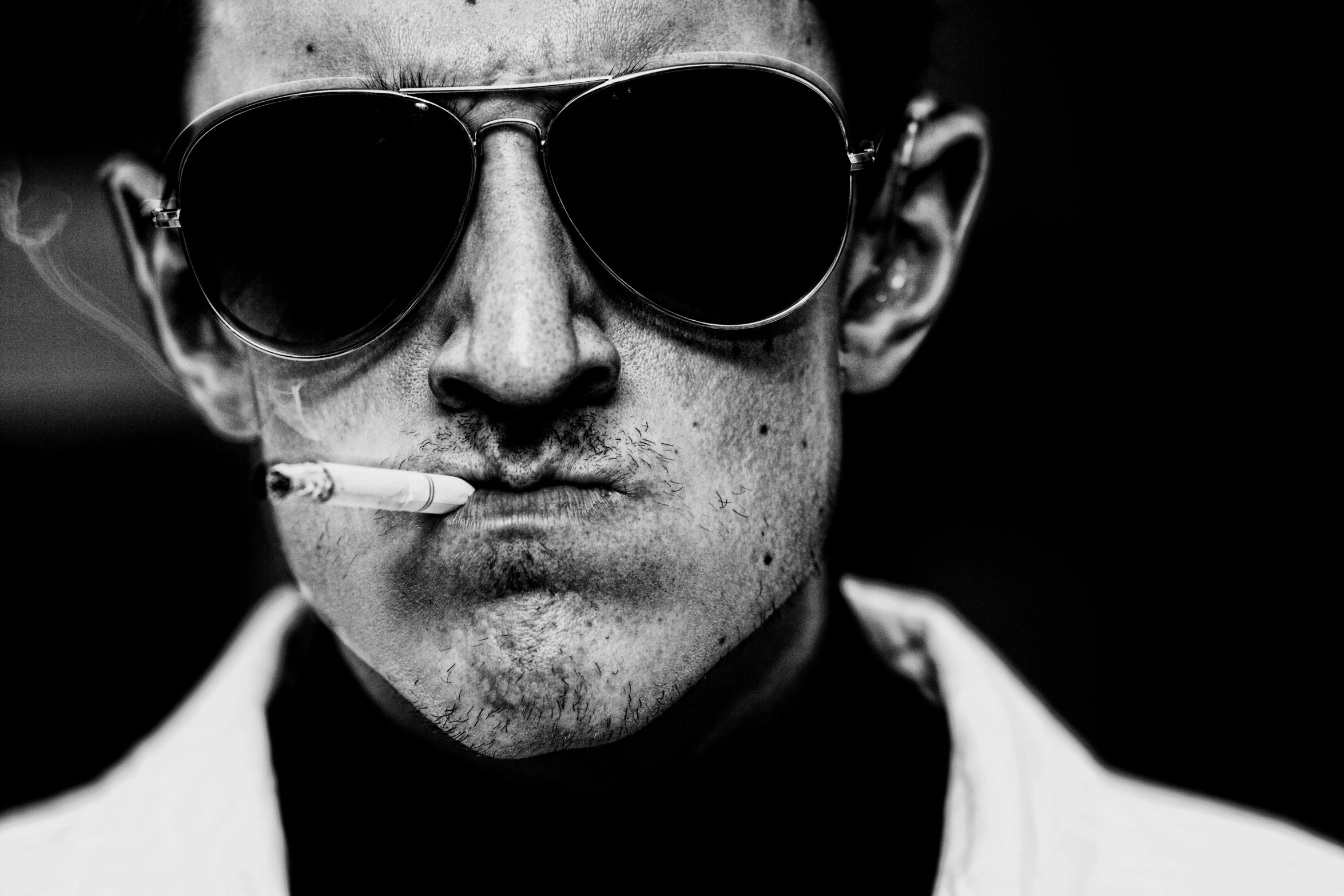 a man wearing a white jacket and dark sunglasses is smoking a cigarette