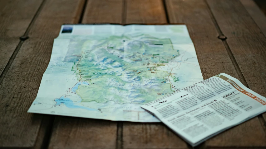 a map on a wood table with a newspaper on the ground