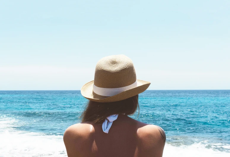 a girl sitting on the beach wearing a hat