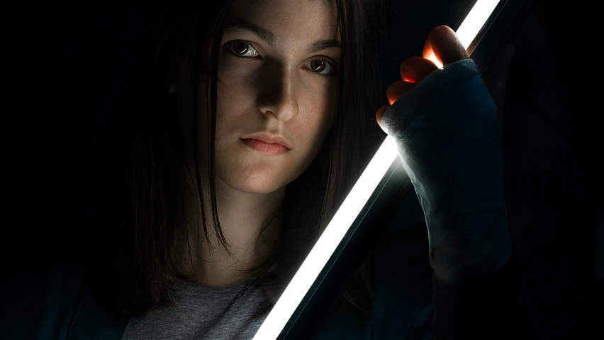 a woman in a dark room holding a glowing light saber