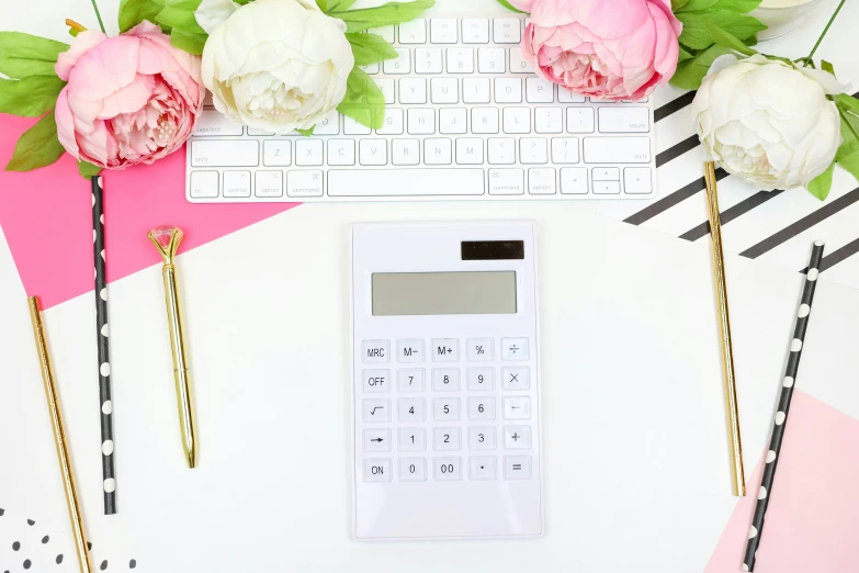 a calculator, two pens and two peonies next to a keyboard