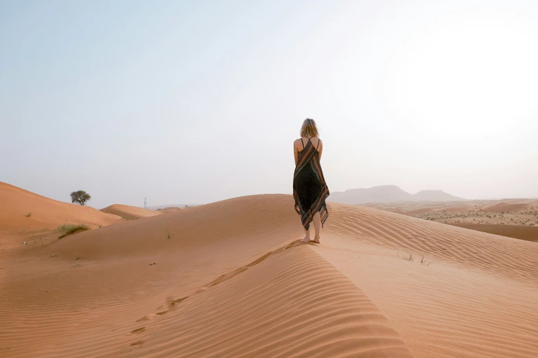 a woman wearing a long dress walks in the sand dunes