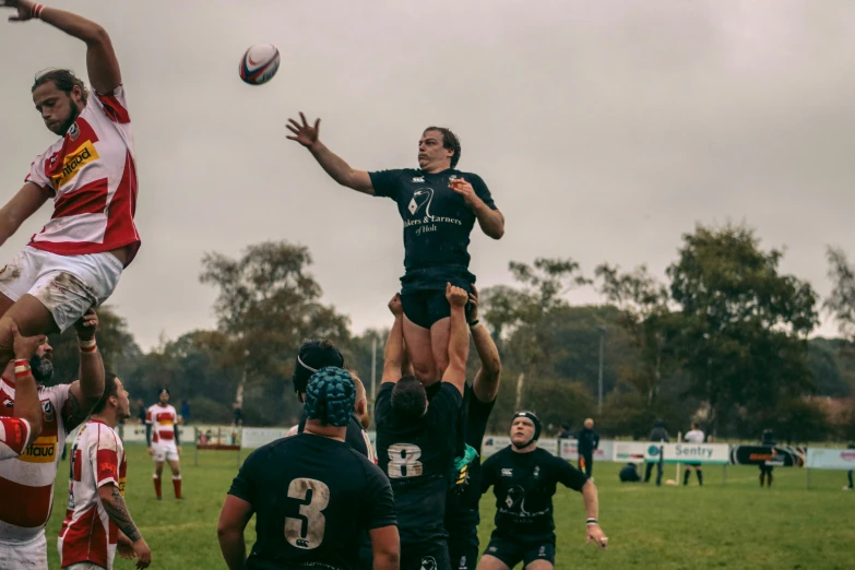 two men jumping to catch a rugby ball while others look on