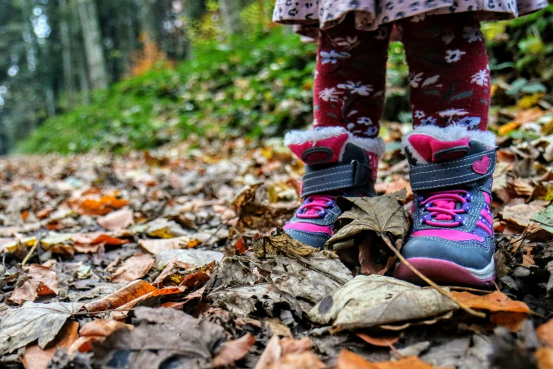 the legs of a child wearing socks and running on leaves in the forest