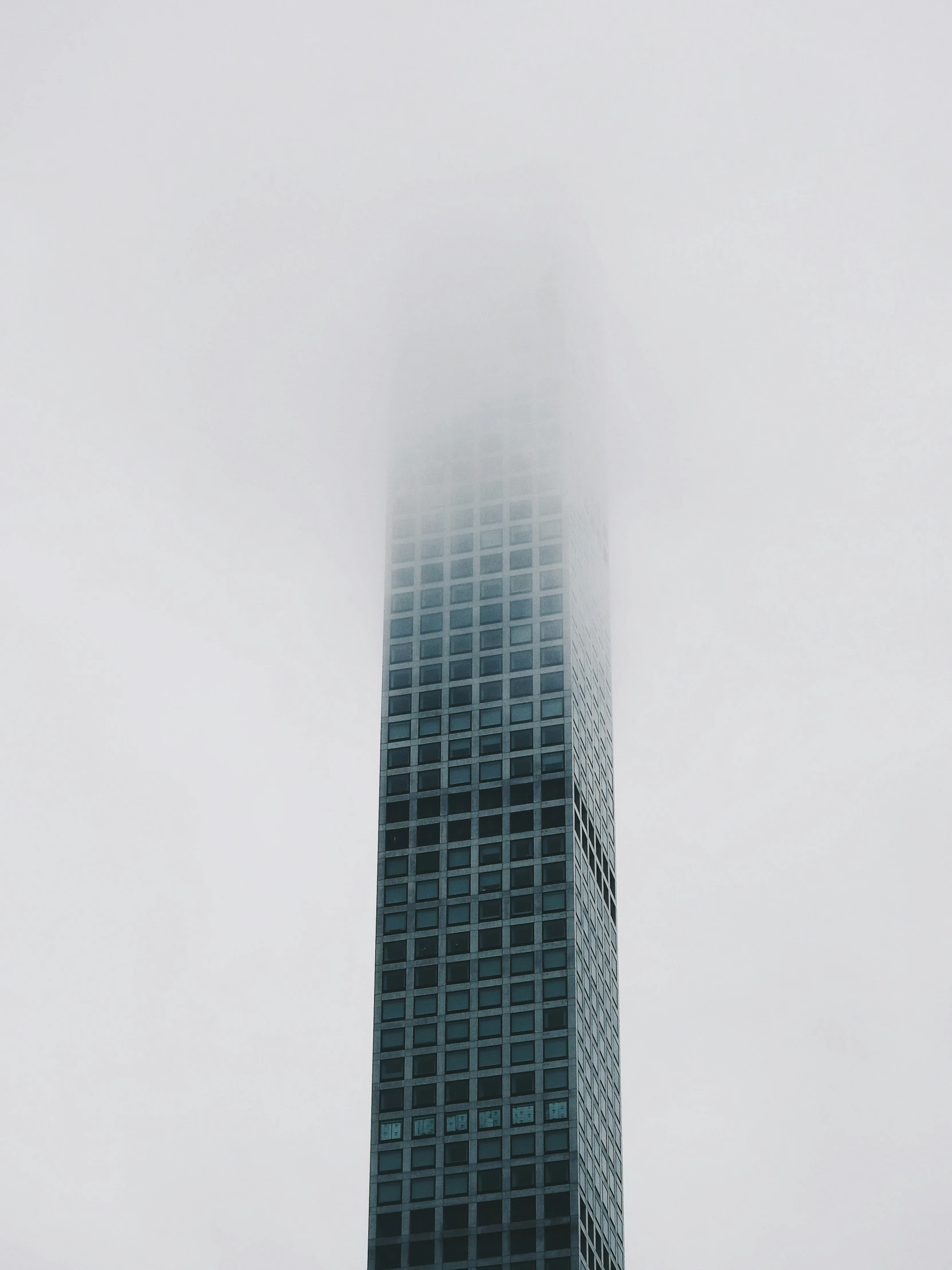 a very tall building in the fog with some clouds