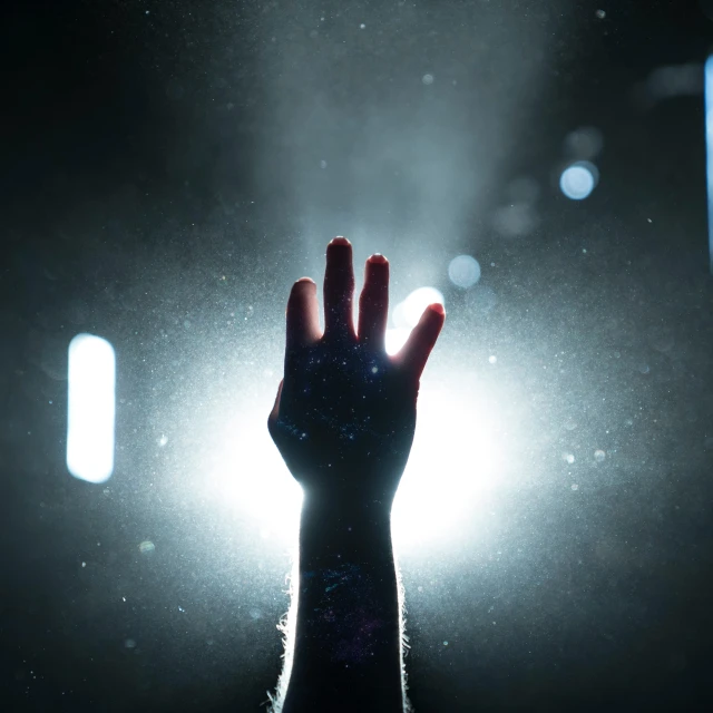 a person's hand in the dark with the sunlight shining down