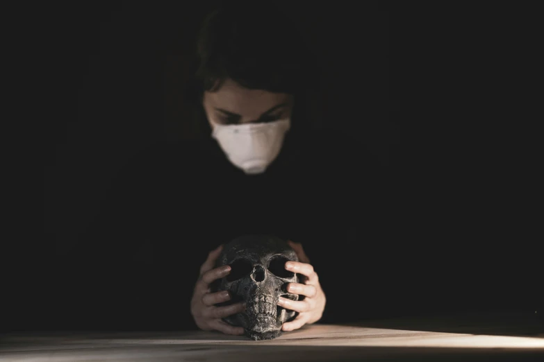 a person wearing a mask sitting in front of a black wall holding a camera