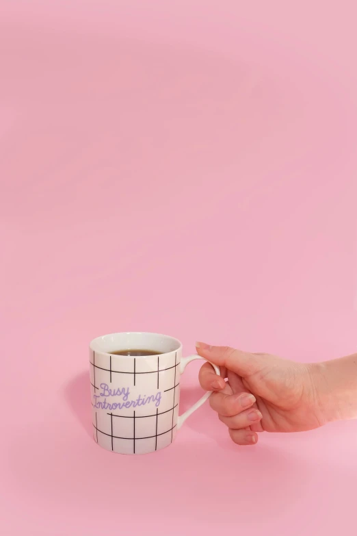 a hand holding a cup with a stick in it on a pink background