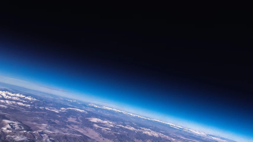 earth with the moon visible above it and snow capped mountains